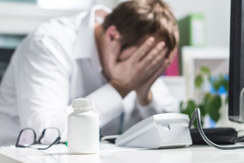 Doctor in white coat holding head in hands in despair or upset