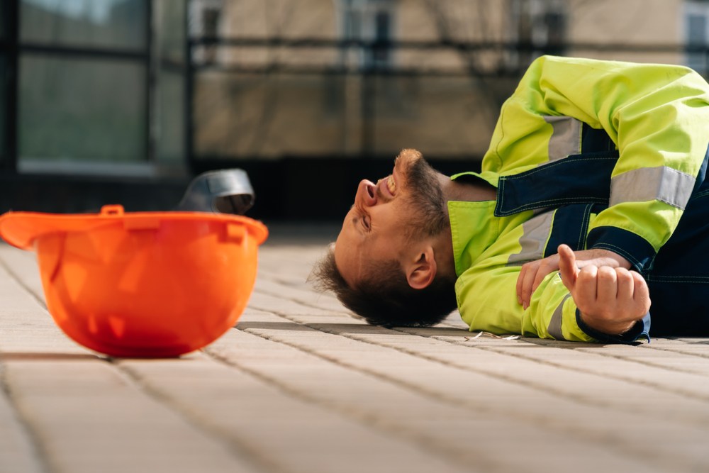 construction worker laying on the ground, holding his arm