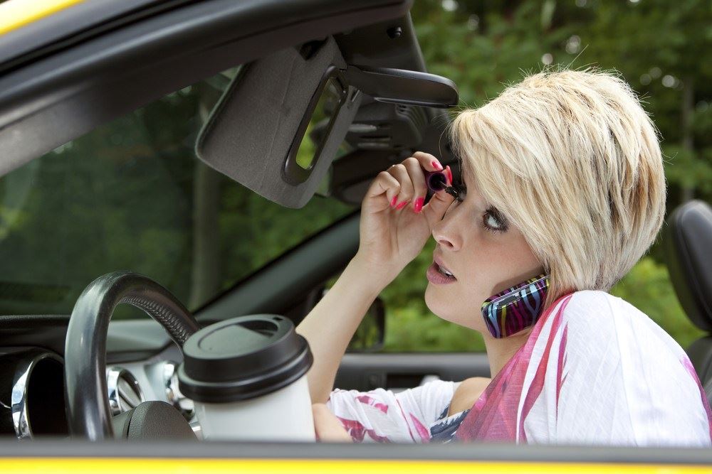 girl on phone doing make-up and having coffee while driving