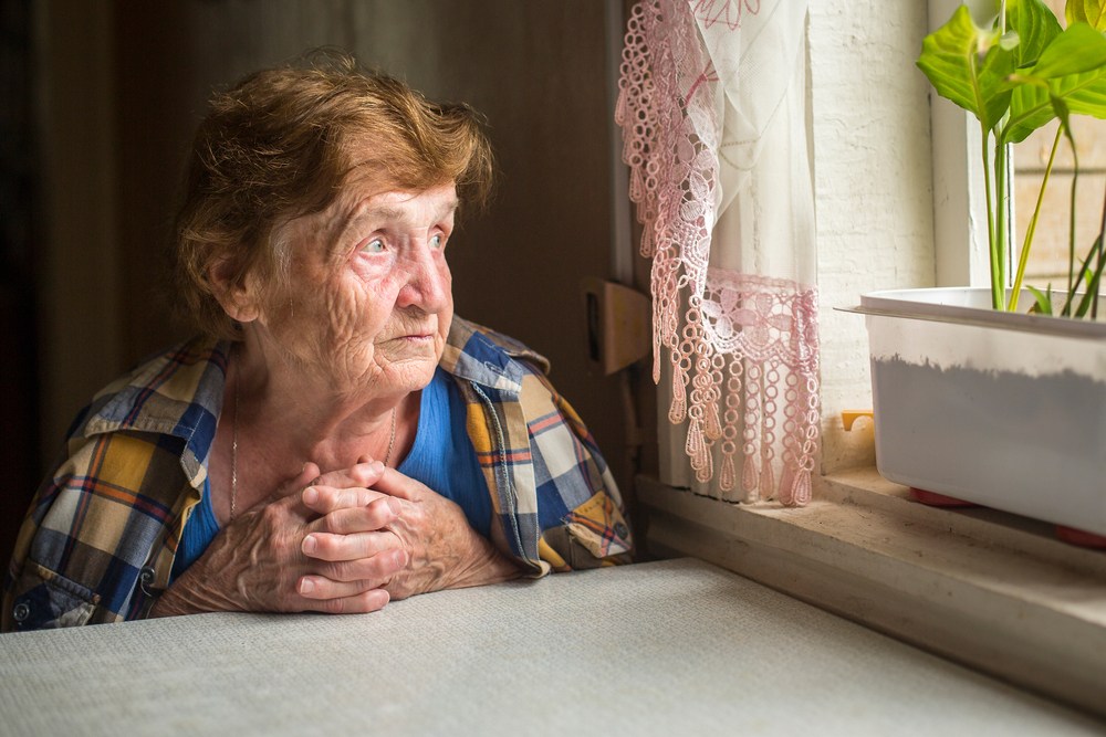 nursing home resident staring out the window with a solemn expression