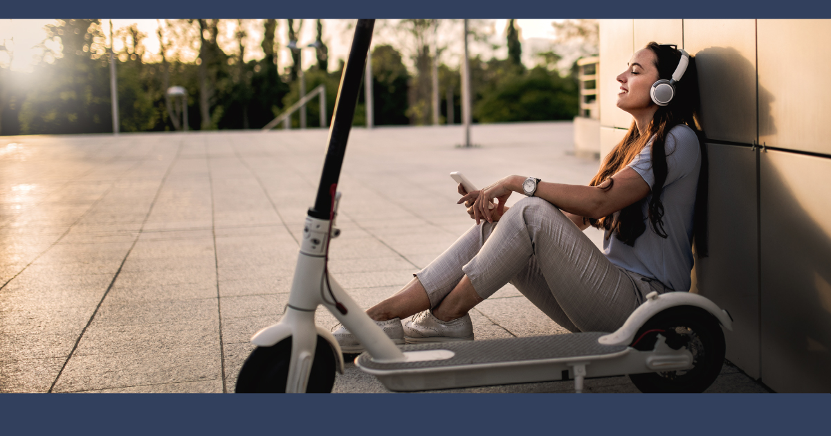 A young woman sits next to an electric scooter.