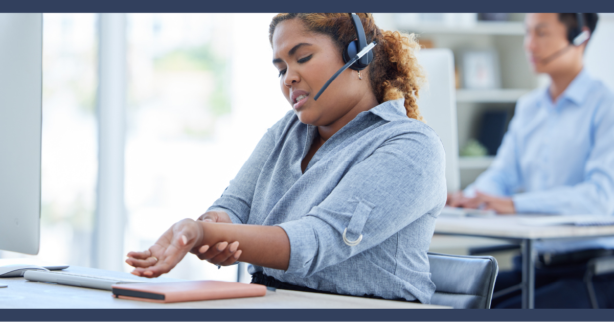 Call center operative sitting at desk clutching their wrist in pain