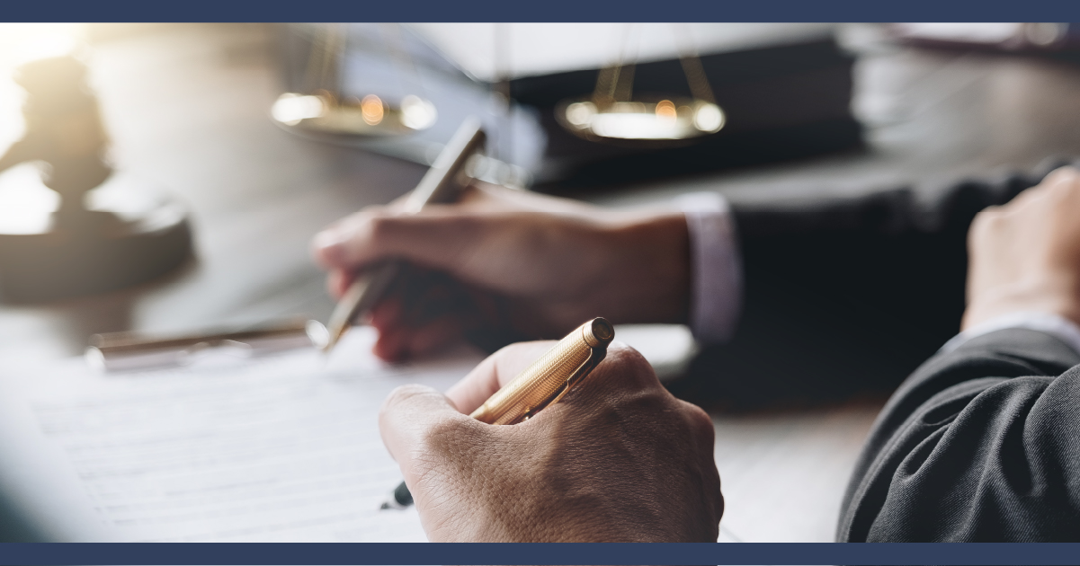 Close up on two people's hands on a desk, writing notes. Background shows legal documents and folders