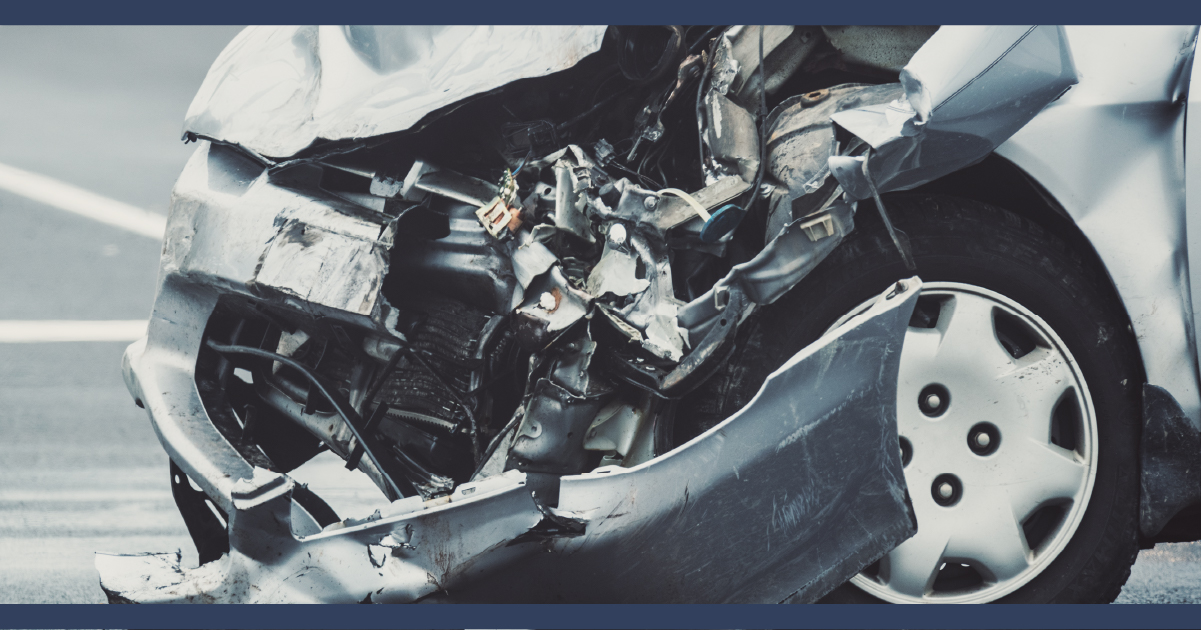 Close up view of the crushed front of a silver car with engine visible and damaged