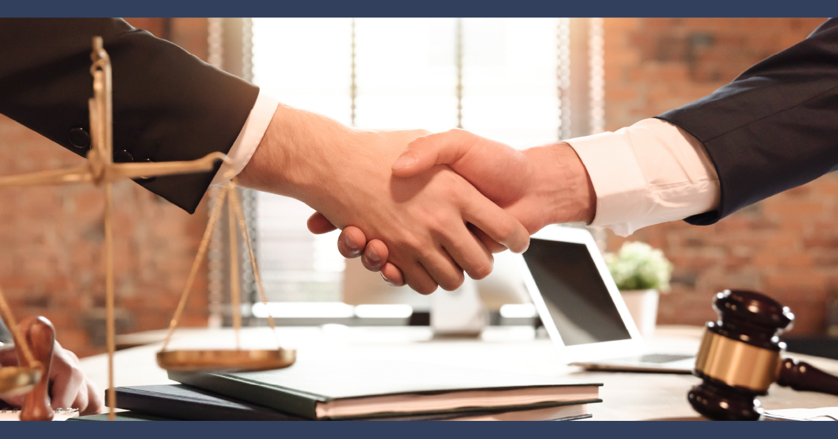Laywer and client shaking hands infront of scales of justice model and a judge gavel on a desk