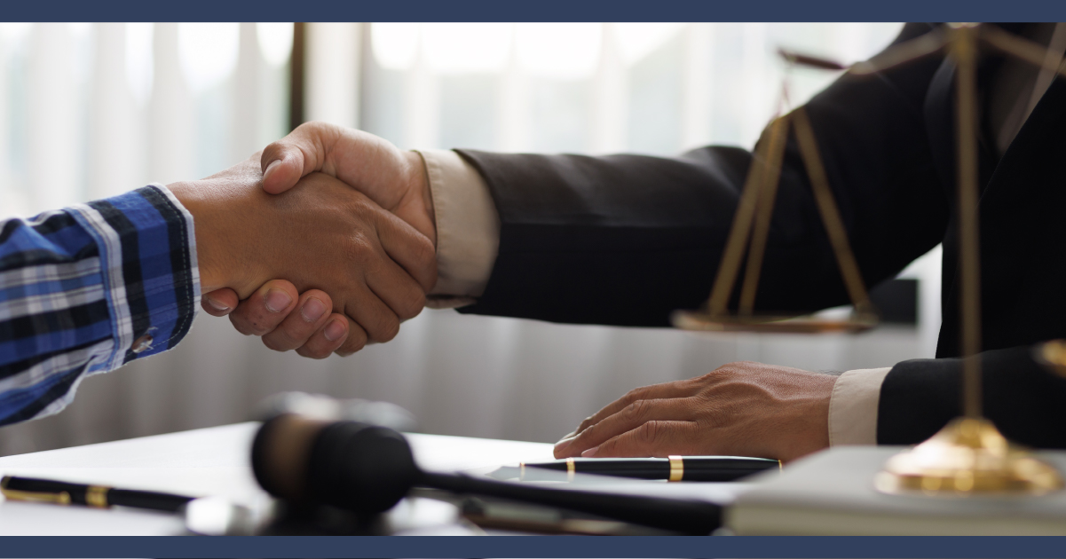 close up of lawyer and client shaking hands, legal paperwork on desk