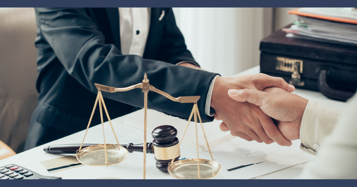 LAwyer and other person shaking hands across a table which is covered in paperwork.
