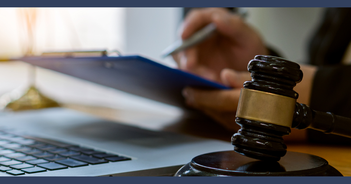 Close up of office desk with judges gavel in foreground and man signing a clipboard document in background