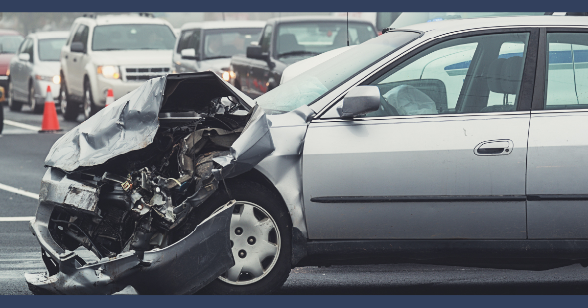 view of a silver car with a buckled and crumpled front bumper and visible engine damage.