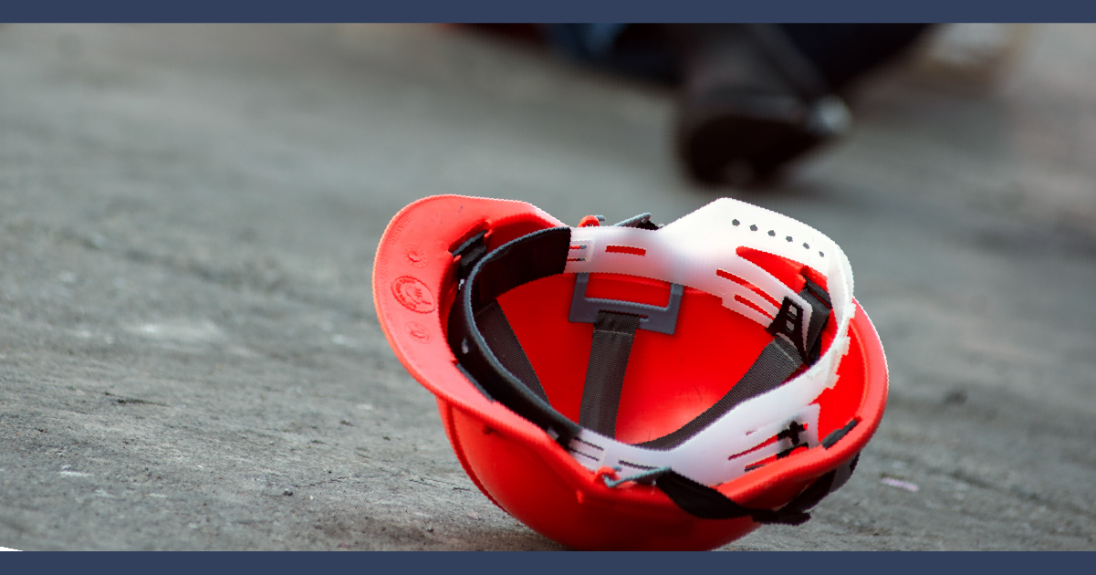 red safety helmet on the floor in the foreground with the legs of someone who has fallen over behind it