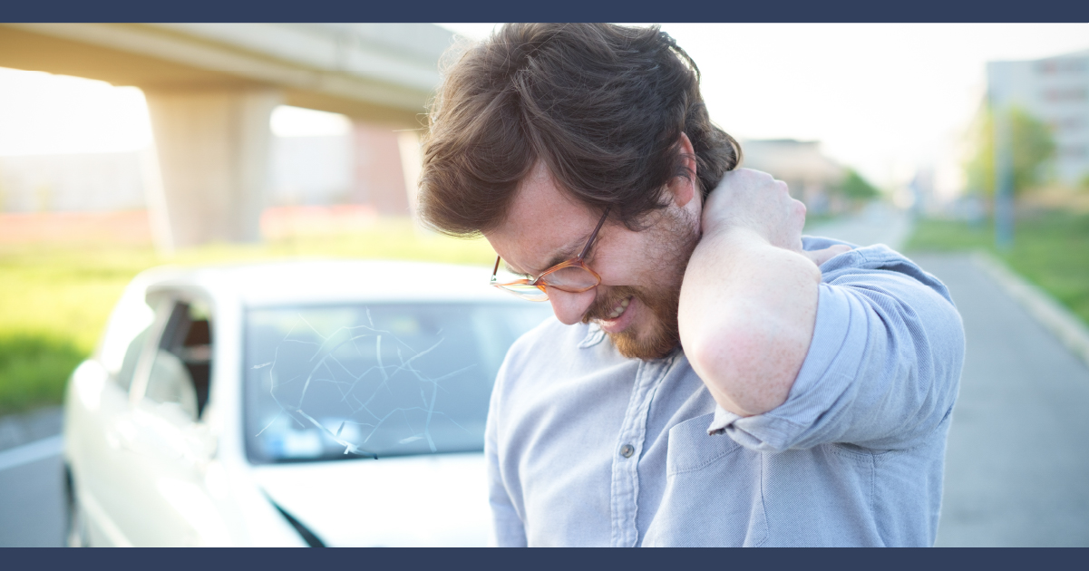 Man nursing an painful neck, with a car parked in background, suggesting it was from a car accident