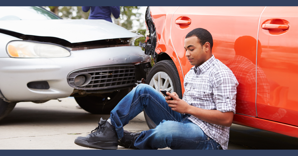 Man sitting on the gorund next to two cars which have been in a road traffic accident