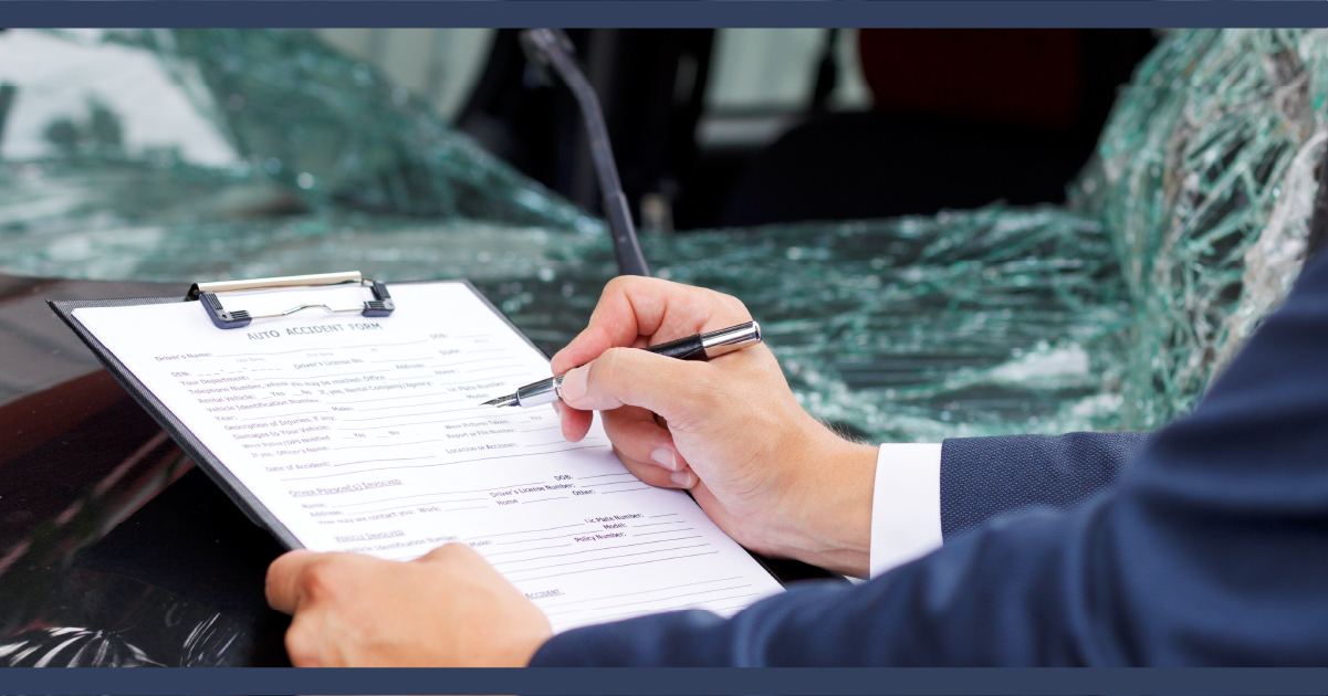 Insurance assessor writing on a clipboard with a crash damaged automobile in the background