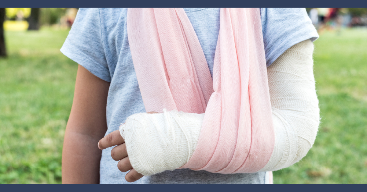 Mid shot of man with arm in a plaster cast and a sling after an injury. Background is green grass.