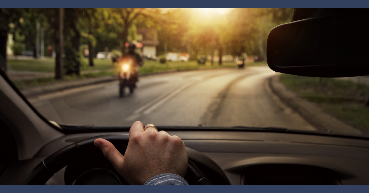 View of the road from the driver position, with motorcycle in foreground and setting sun in background