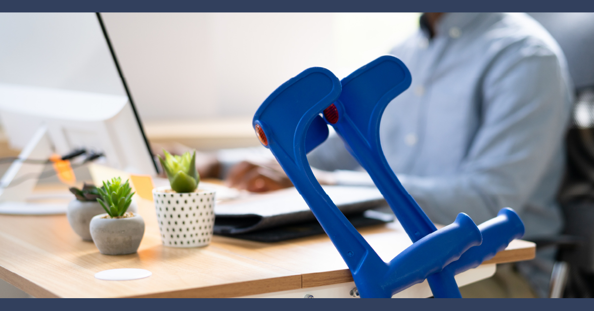 man at desk working on computer, with crutches in foreground resting against his desk
