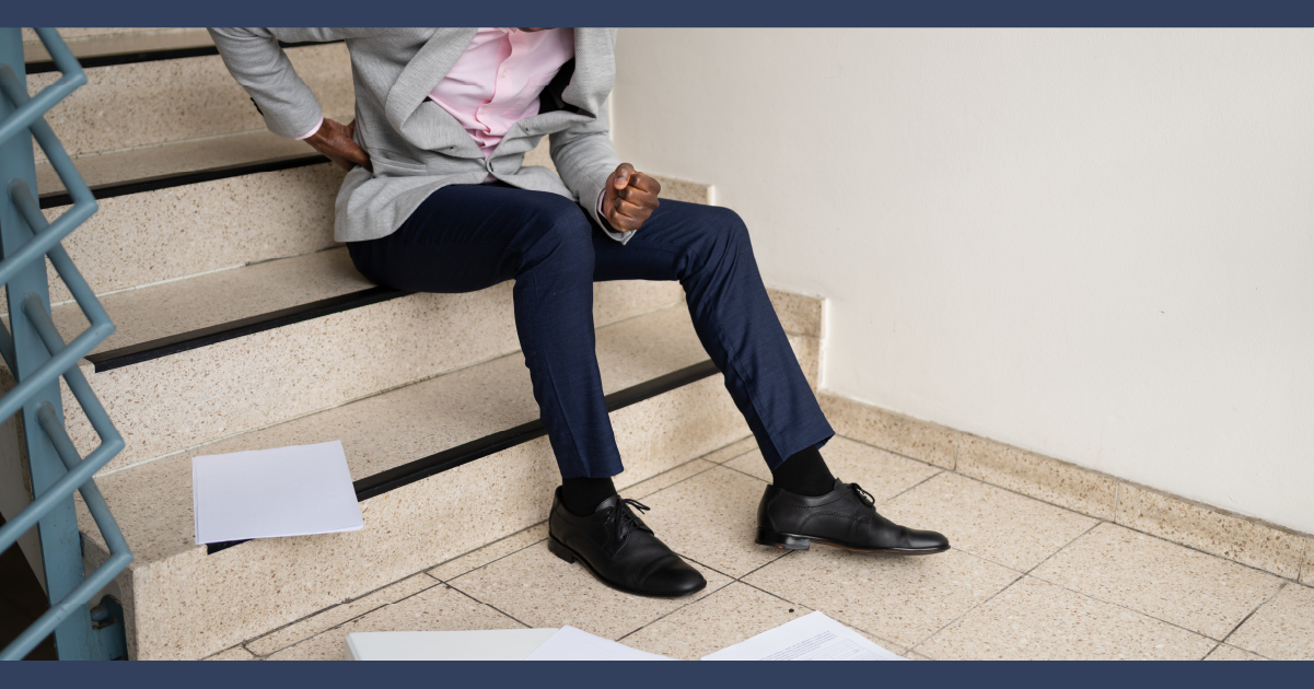 Close up on man sitting on stairs, rubbing his back, surrounded by paperwork as if he slipped and dropped the documents