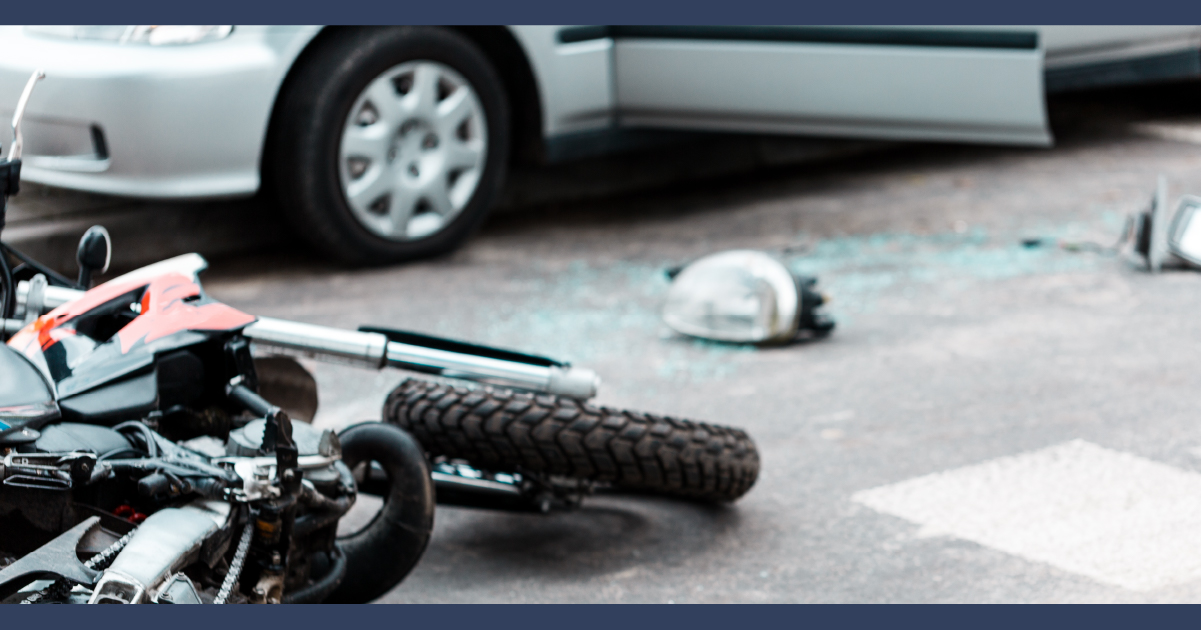 Motorcycle on the ground next to a dented car. Motorcycle helmet and broken glass enarby