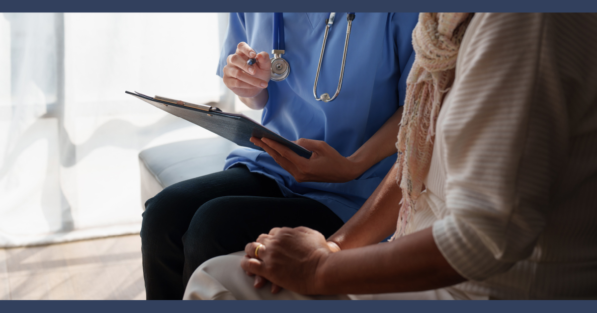Medical technician holding a clipboard sitting next to a person who is wearing a yellow outfit who is clutching their hands together