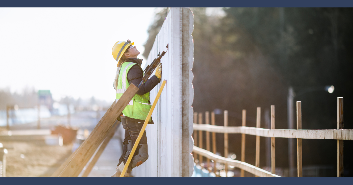 person in hi-vis jacket and construction hard hat inspecting a wall