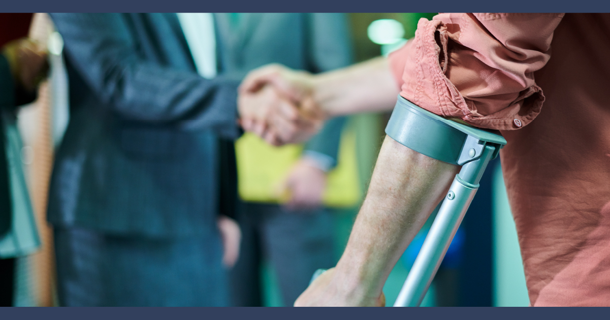 Man in blue suit shaking hands with a man on crutches in an office environment
