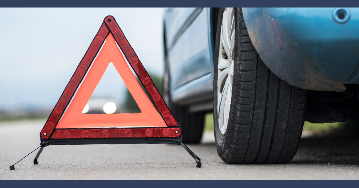 Triángulo de advertencia rojo en la carretera junto a un auto azul