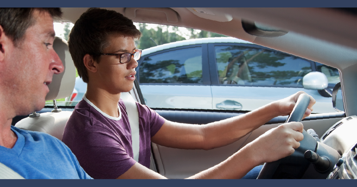 Teenager at wheel of car with adult next to them instructing them on how to drive