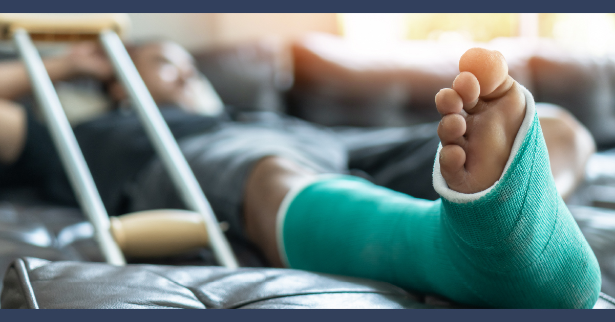 Man lying on hospital bed with leg in cast and with a walking crutch