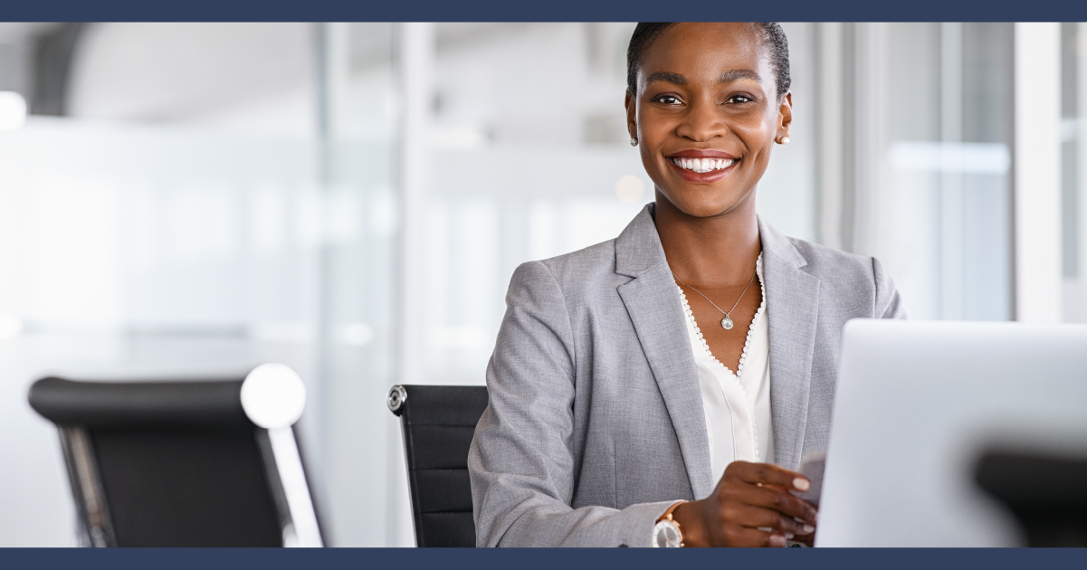 Lady sitting at desk in a suit, with an welcoming smile