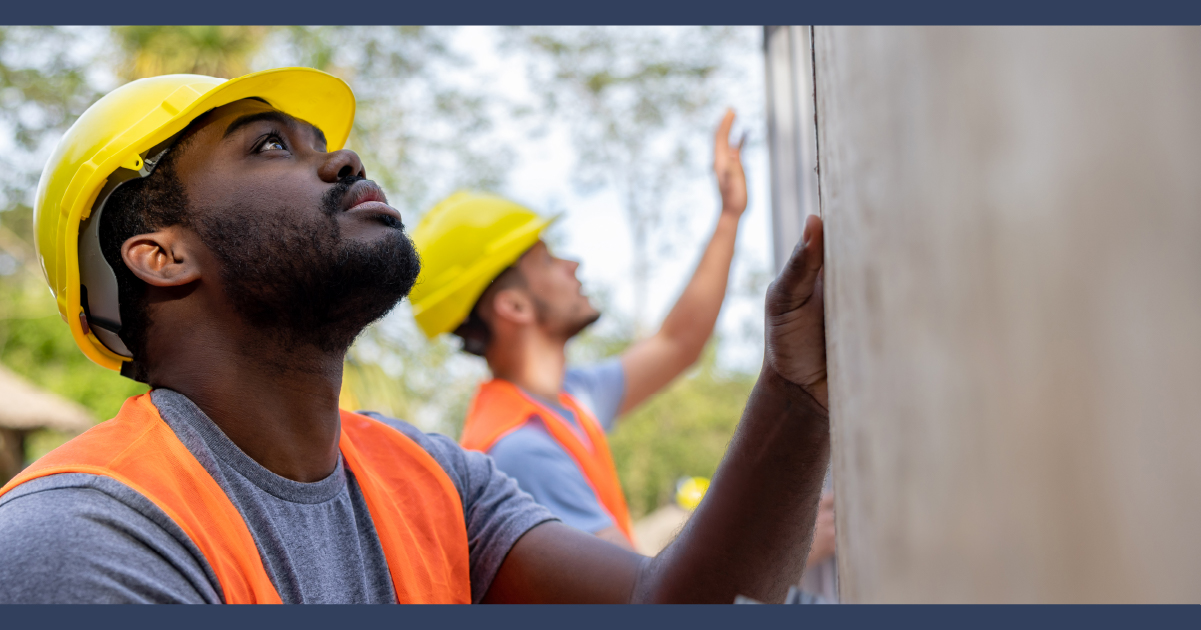 Two men in hi-vis and safety hats moving a panel