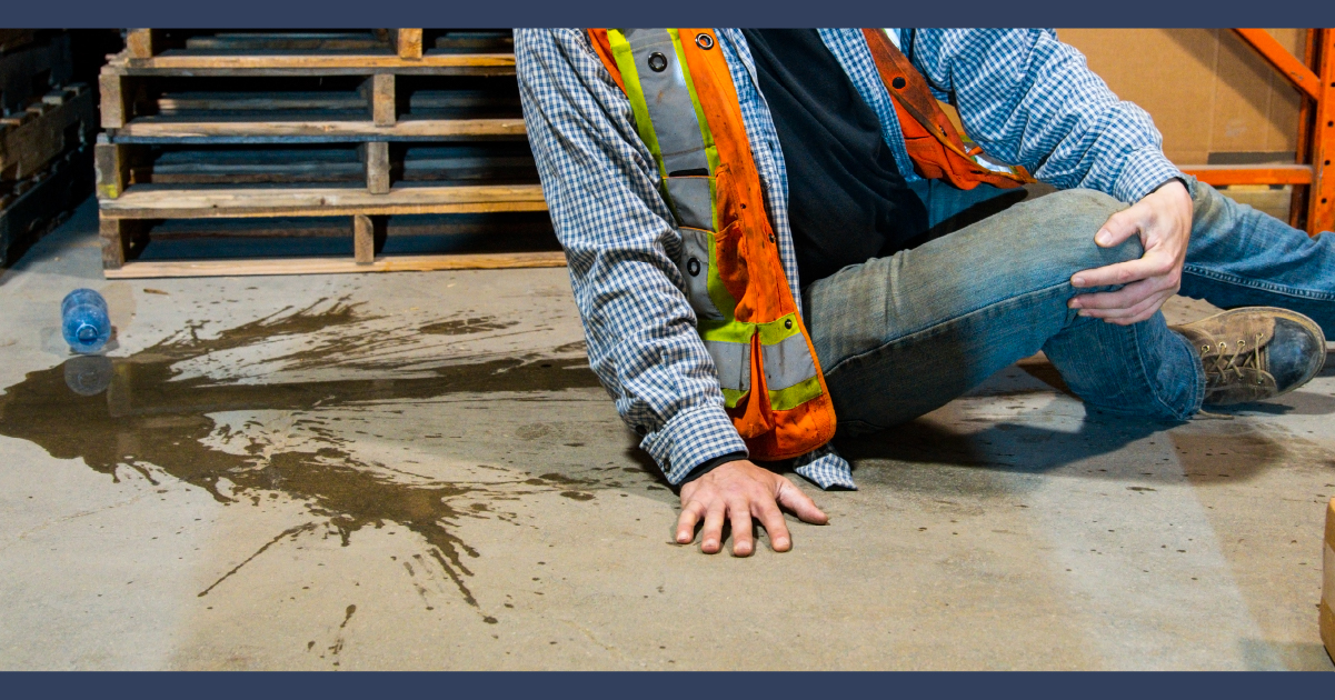 Am n in hi-vis jacket on the floor near some metal rails and steps, with spilt liquid beside him.