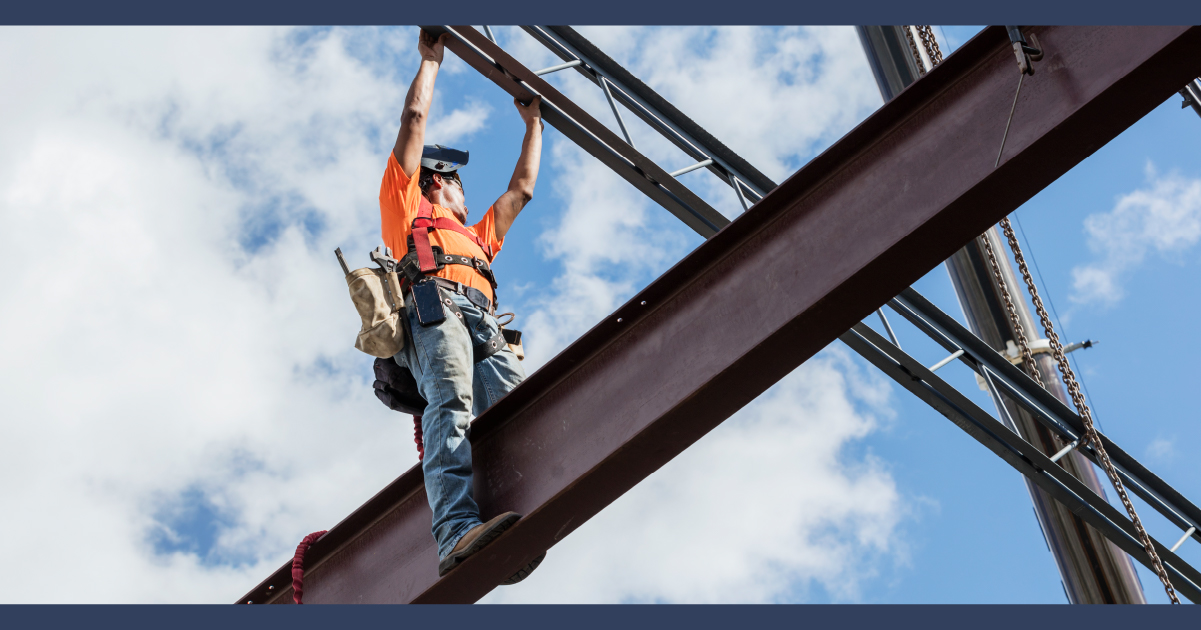 Trabajador de la construcción sobre una viga de soporte con una chaqueta naranja brillante.