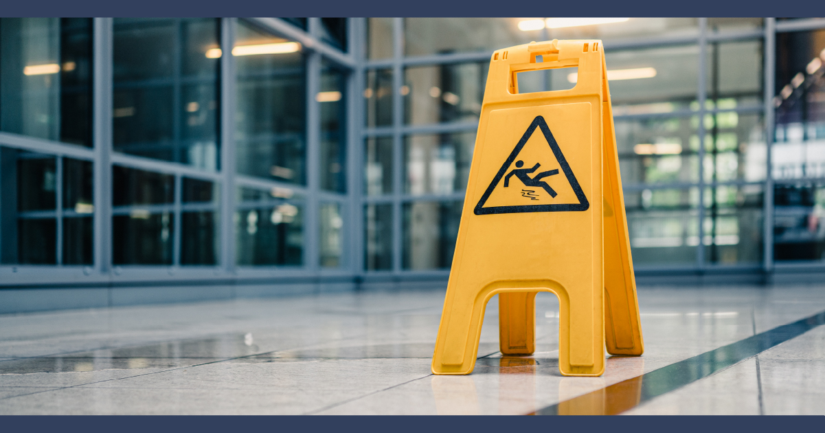 wet tiled floor on commercial property with a yellow warning sign by a wet area