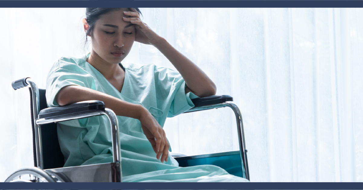 Woman in wheelchair and wearing green medical gown looking unhappy