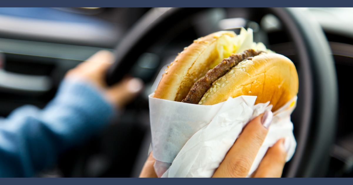 Man holding a hamburger while driving a truck one handed