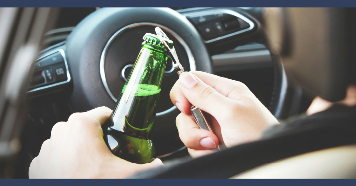 Person opening a ber bottle while in the driver seat of a car